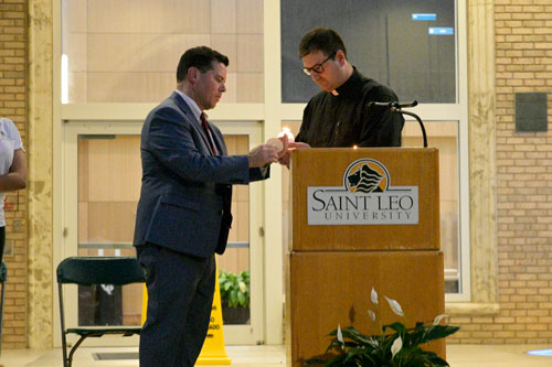 Father Kyle Smith, university chaplain lights the candle of University President Jeffrey D. Senese